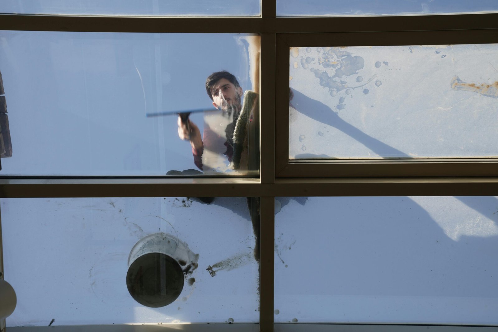 A male window cleaner washing the exterior glass roof from above with a tool during daylight.
